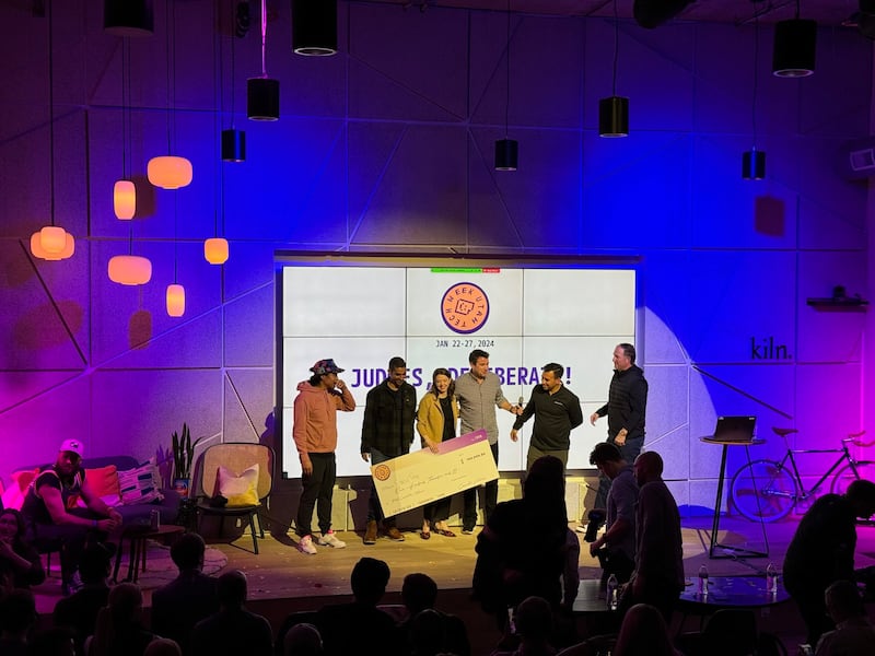Utah Tech Week Pitch Competition winner Jennie Moser (of Stagetime) and runner-up Luis Benavides (of Neighborbrite) stand onstage at Kiln with Utah Tech Week co-founder Trent Mano and pitch competition judges.